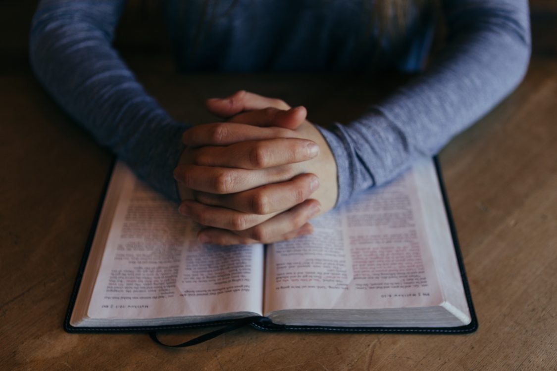 betende Hände auf einer geöffneten Bibel